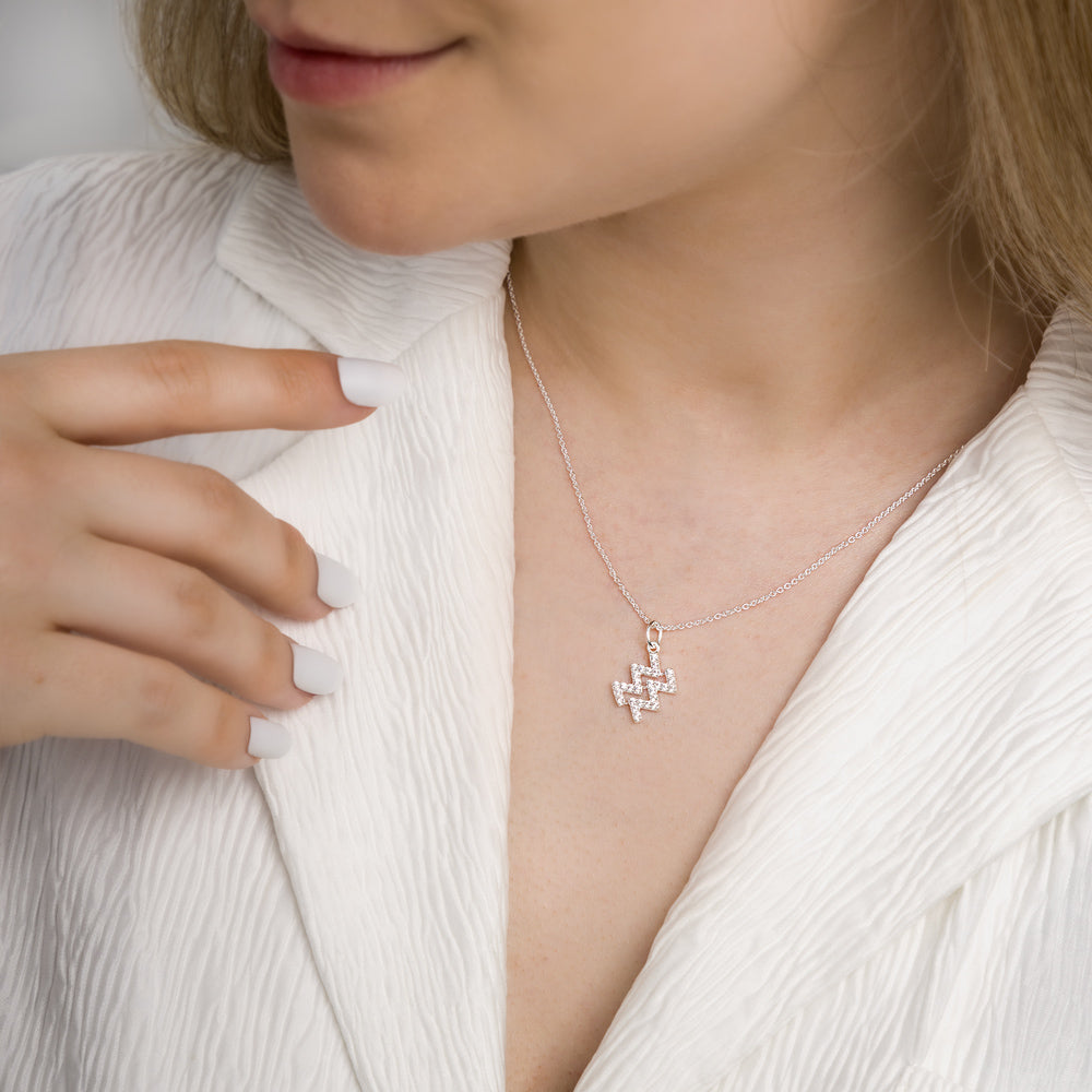 Woman wearing aquarius zodiac necklace around her neck in white top.