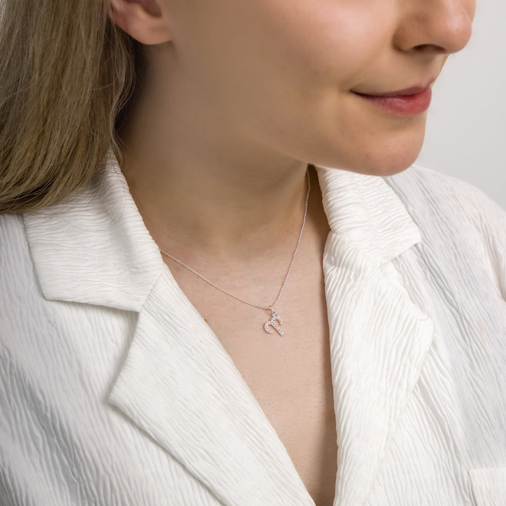 Woman wearing aries zodiac necklace around her neck in white top.