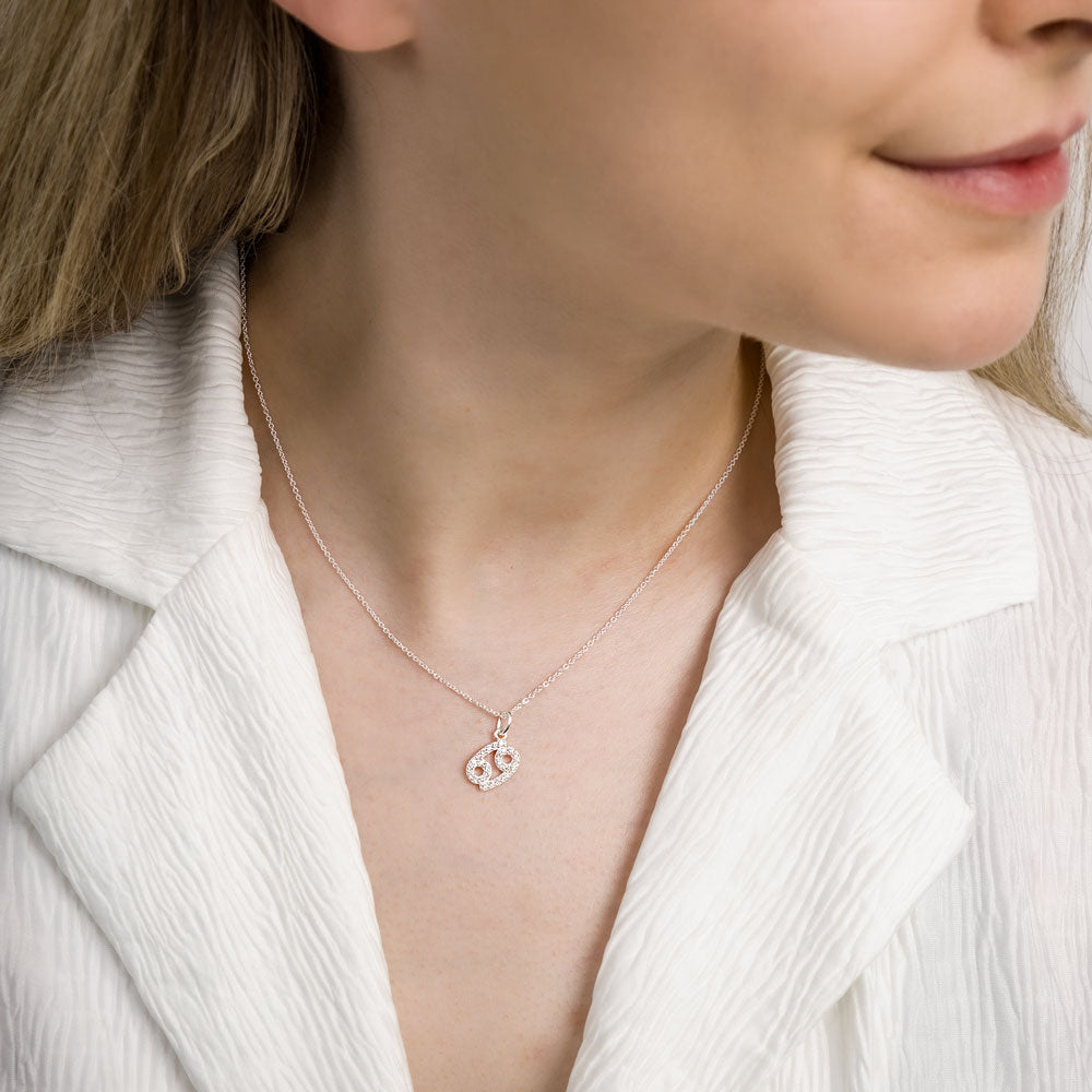 Woman wearing cancer zodiac necklace around her neck in white top.