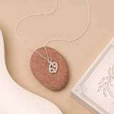 Flat lay of necklace with zodiac pendant on beige background and white details. 