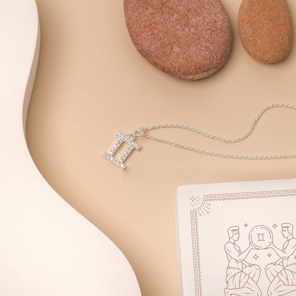 Flat lay of necklace with zodiac pendant on beige background and white details. 