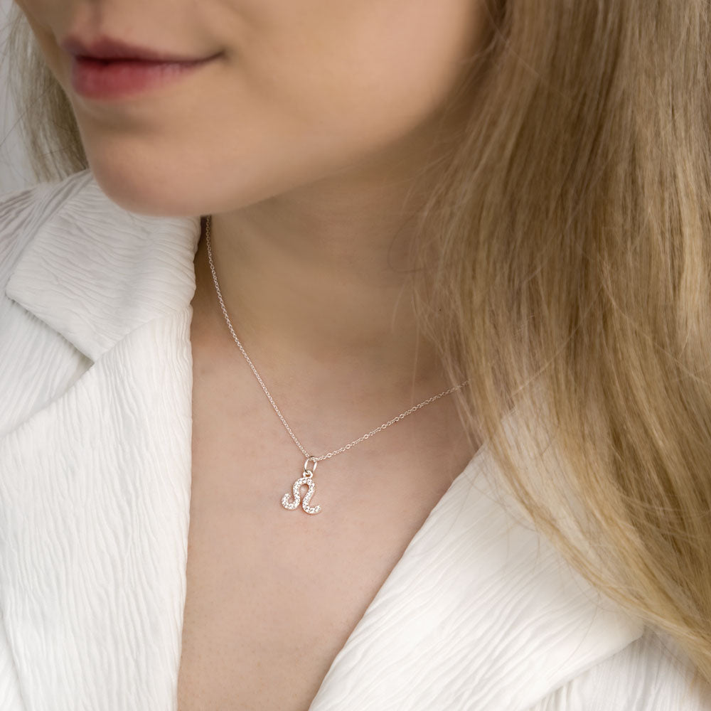 Woman wearing leo zodiac necklace around her neck in white top.