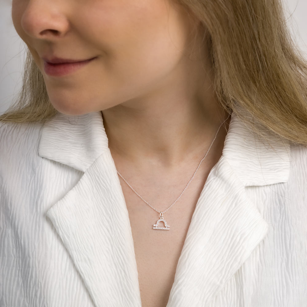 Woman wearing libra zodiac necklace around her neck in white top.