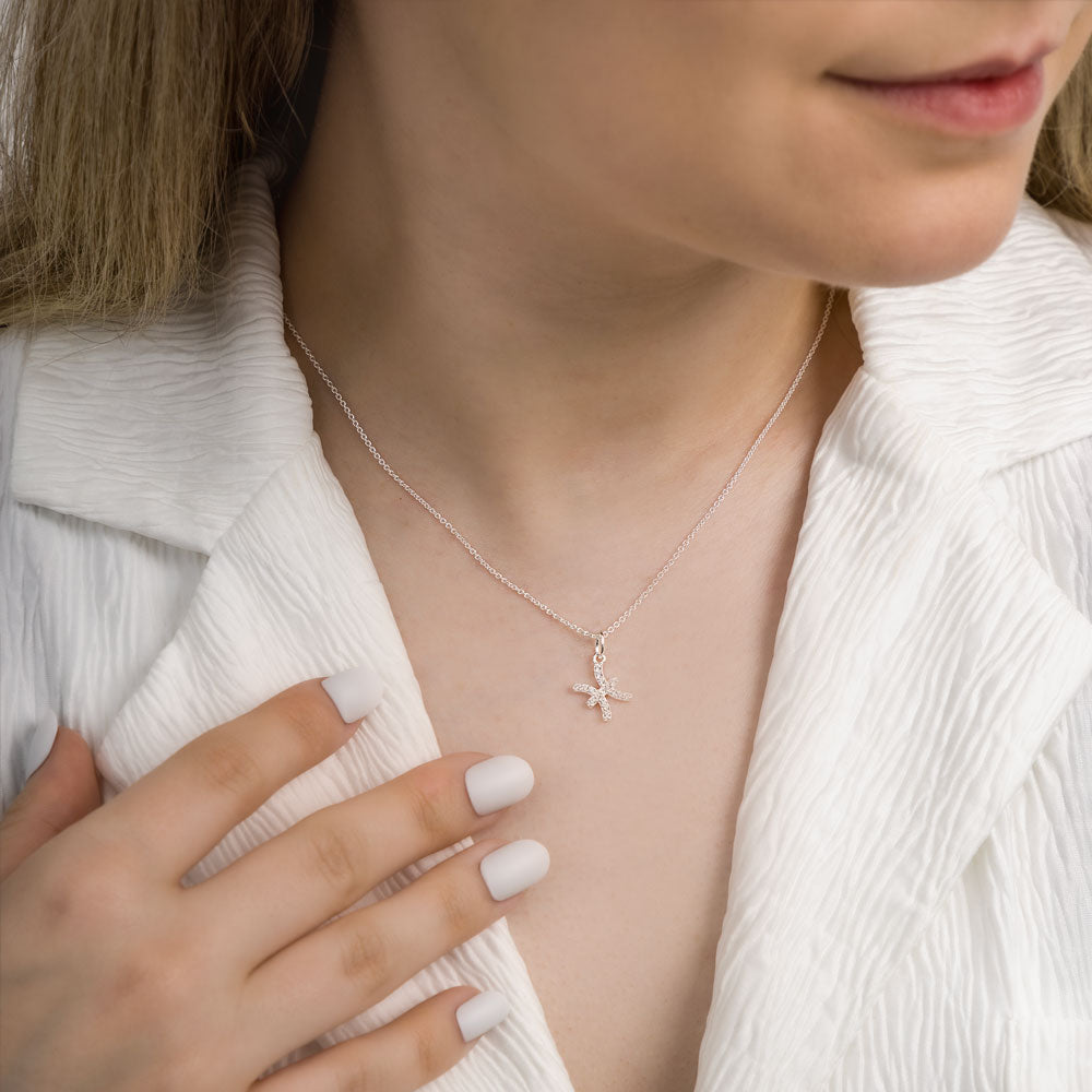 Woman wearing pisces zodiac necklace around her neck in white top.