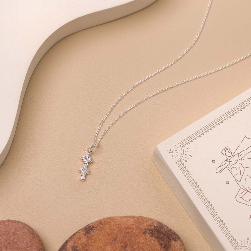 Flat lay of necklace with zodiac pendant on beige background and white details. 