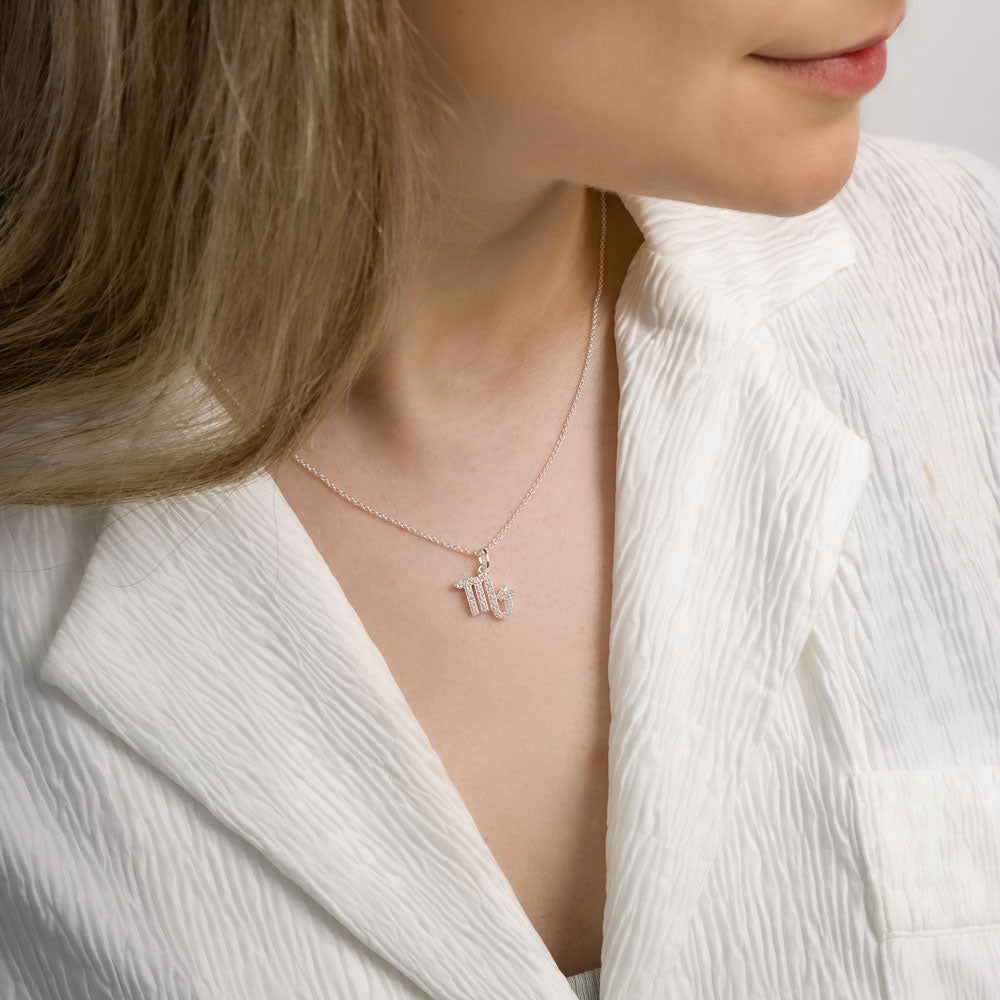 Woman wearing scorpio zodiac necklace around her neck in white top.