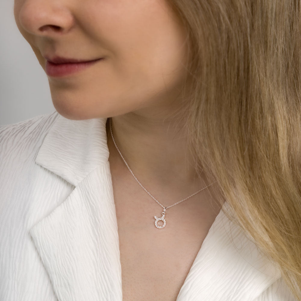 Woman wearing taurus zodiac necklace around her neck in white top.