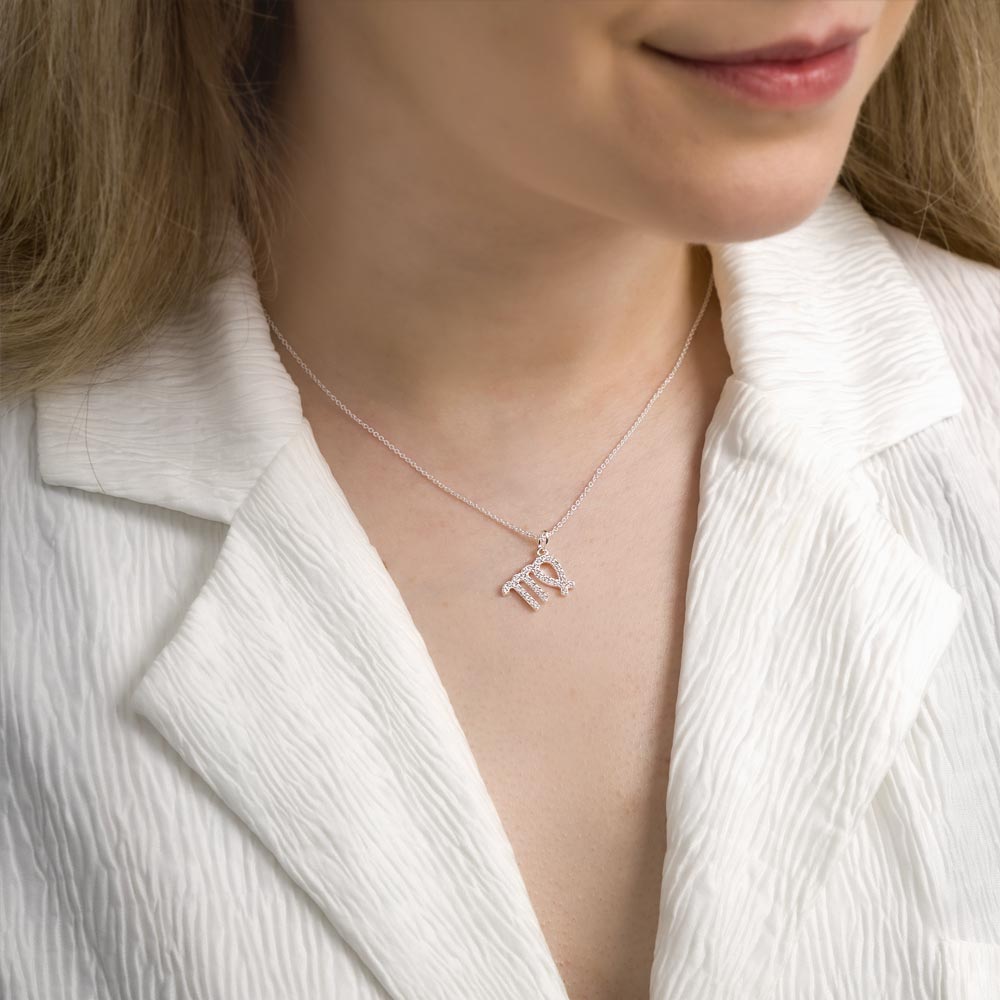 Woman wearing virgo zodiac necklace around her neck in white top.