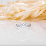 Silver engagement ring with CZ stone in 6mm placed on a white and beige surface.