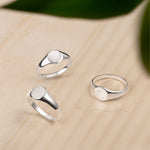 Marketing image of three flat signet silver rings placed against beige background. 