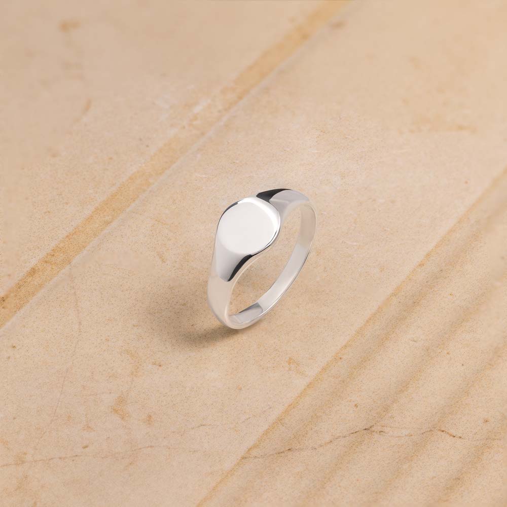 Women's Signet ring in broad flat design in sterling silver standing against beige background. 