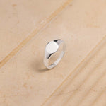 Women's Signet ring in broad flat design in sterling silver standing against beige background. 