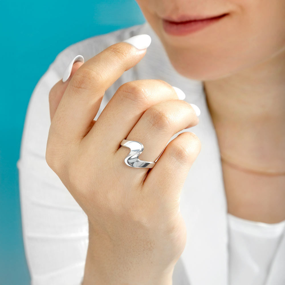 Woman wearing silver wave ring against white blouse. 