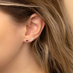 Close-up of a woman's ear wearing two earrings: a small stud earring featuring a ruby birthstone and a stunning Cancer constellation-shaped piece with clear stones