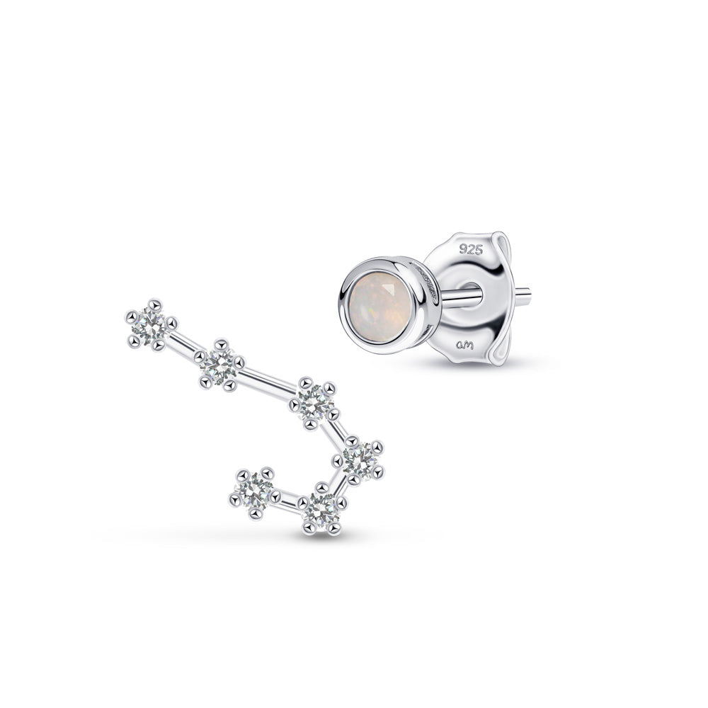 Close-up of two pieces of silver jewelry. One is a stud earring adorned with a Gemini birthstone; the other is a curved earring with a series of small clusters, reminiscent of constellations.