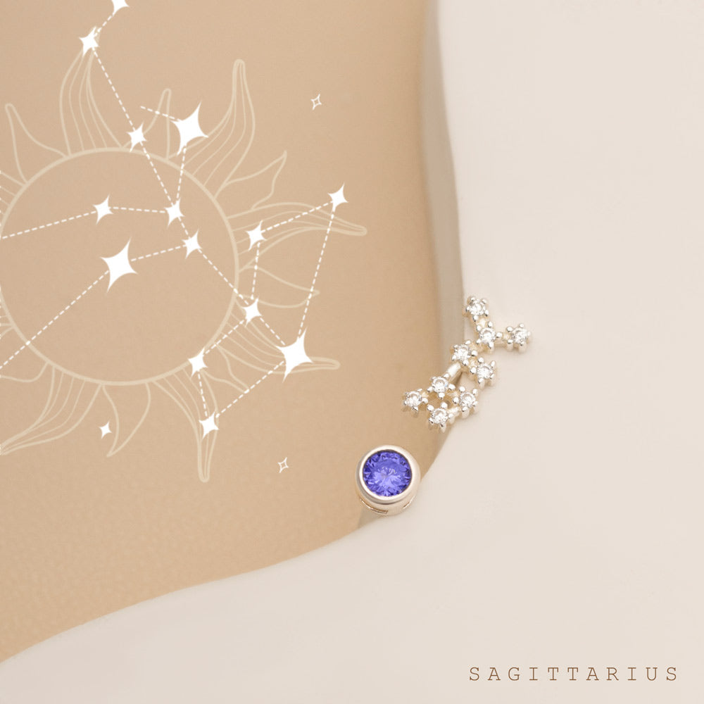 A Sagittarius constellation illustration is surrounded by a sun-like design, Next to it is a pair of silver constellation studs, each featuring Sagittarius birthstone blue gemstones and small white stones arranged like constellations.