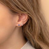 Close-up of a woman's ear wearing two earrings: a small stud earring featuring a sapphire birthstone and a stunning Virgo constellation-shaped piece with clear stones