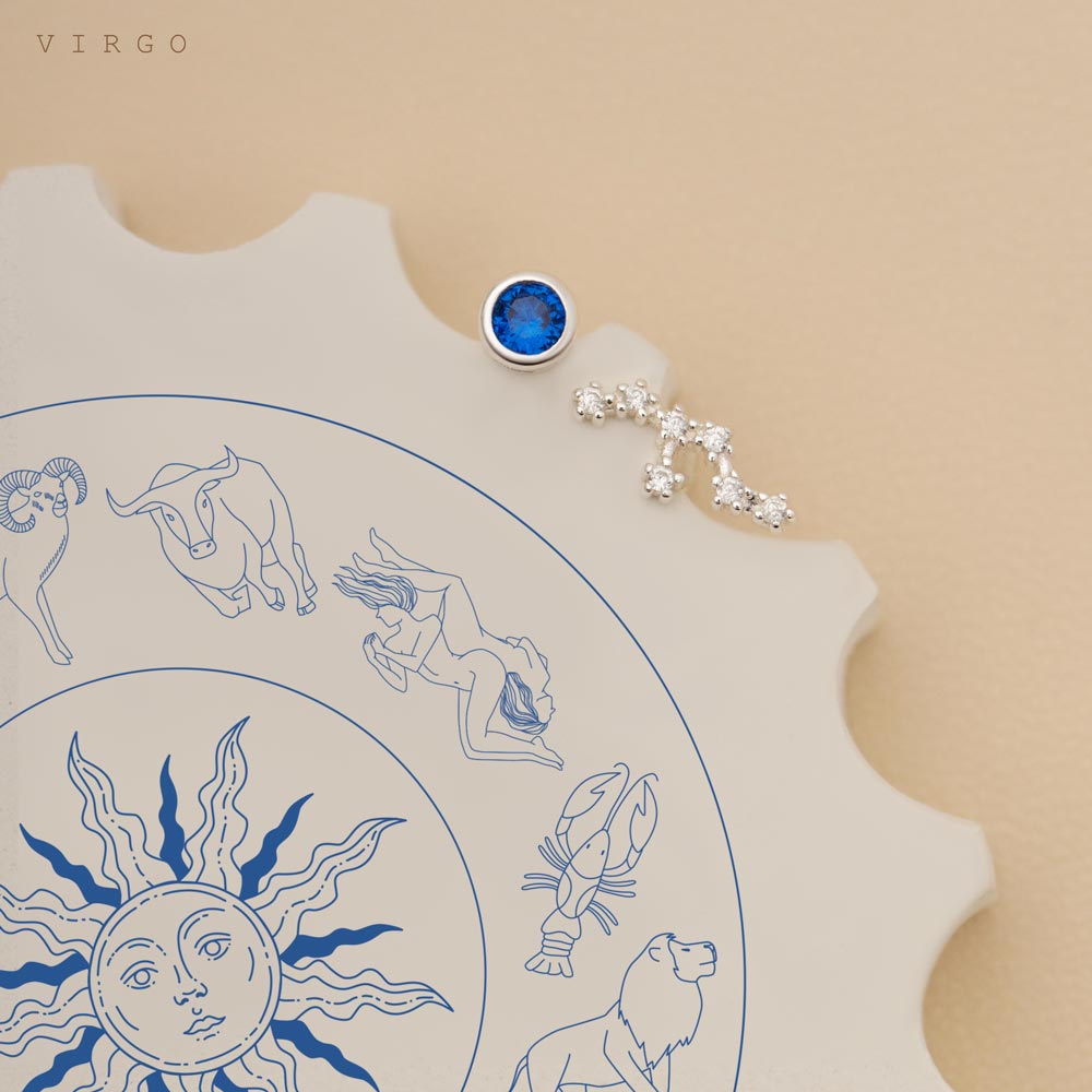 A pair of constellation studs, One earring features a blue gemstone, and the other has a constellation. The chart displays zodiac symbols and illustrations, with the Virgo symbol prominently visible as its birthstone glimmers subtly.