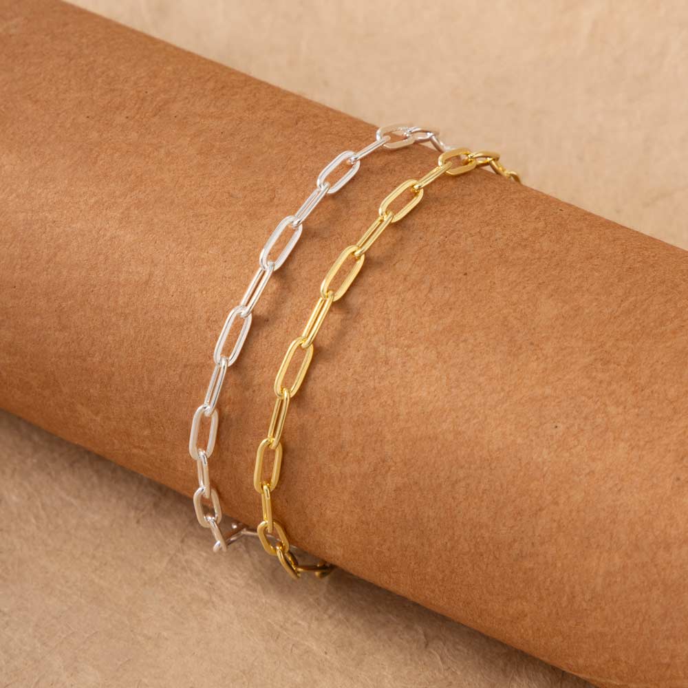 a pair of gold plated and silver paperclip bracelets placed on a brown surface