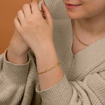 A close-up of a woman's hand wearing a paperclip bracelet with matching necklace