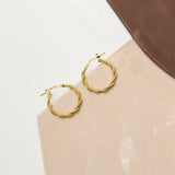 Marketing image of Gold plated Textured Hoops with post notch againts beige-brown tile.