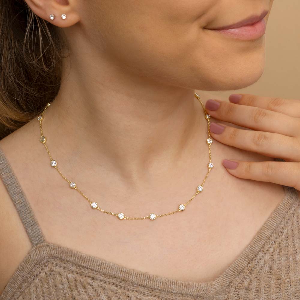 A woman wearing gold plated CZ charm necklace around her neck in brown top