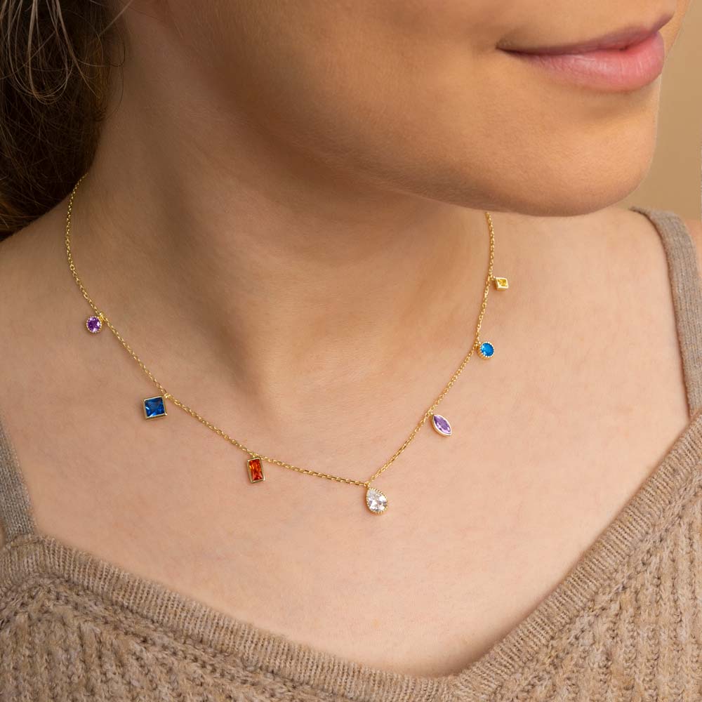 A woman wearing gold plated rainbow  multi shapes hanging charm pendant necklace around her neck in brown top