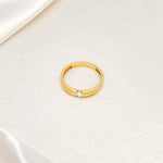 Gold plated solitaire wedding band with CZ stone in 3mm placed on a beige surface.