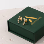 Two elegant gold crawler earrings featuring cubic zirconia on a green box against a beige background