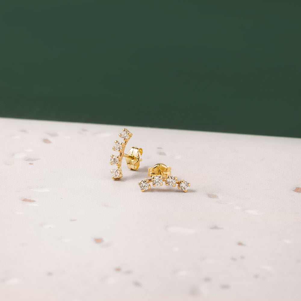 Two elegant gold crawler earrings featuring cubic zirconia against a beige and green background