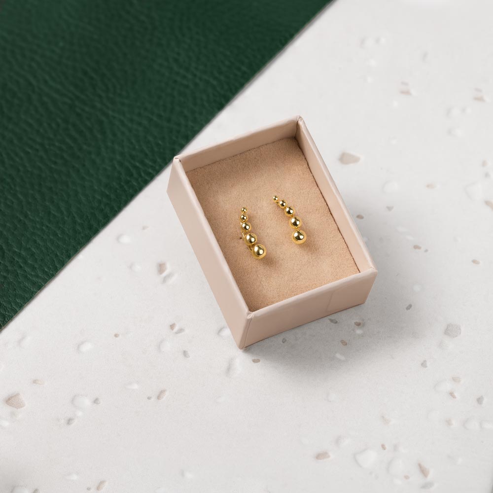 An elegant gold balls crawler earring in a beige box against a white and green background