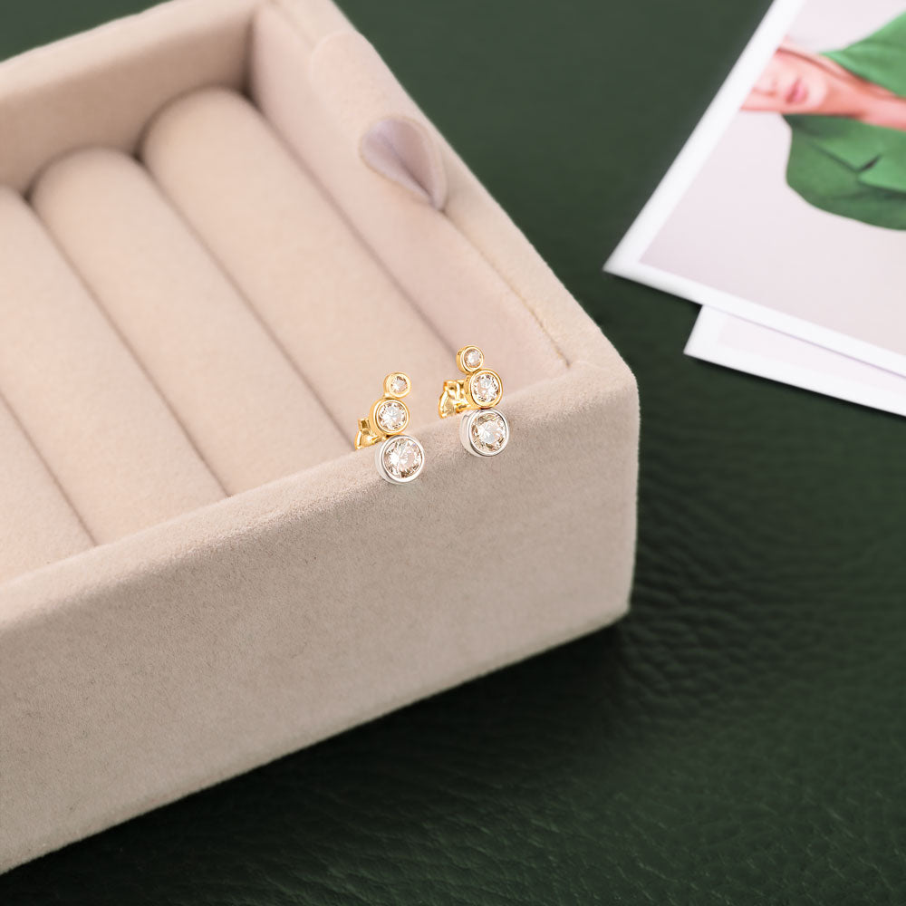 Two elegant yellow and white gold crawler earrings featuring cubic zirconia against a beige and green background