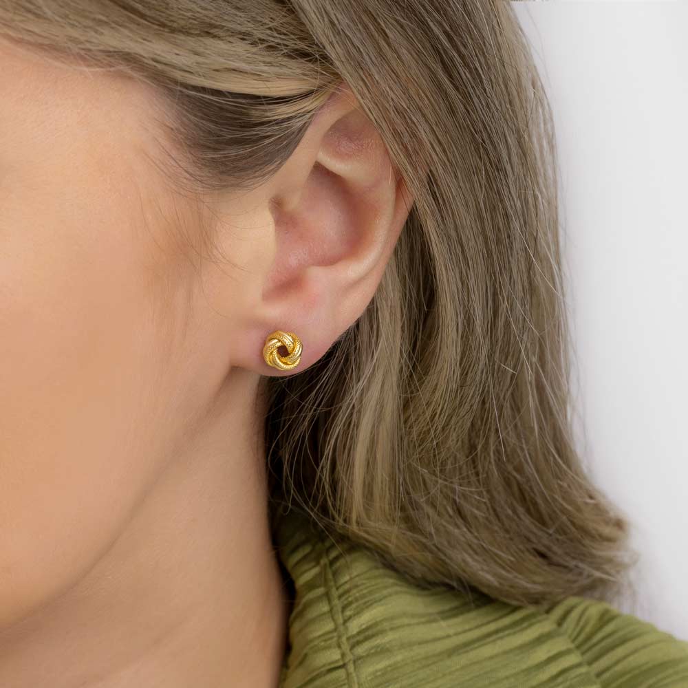  Close up picture of a woman's ear wearing gold knot studs earring