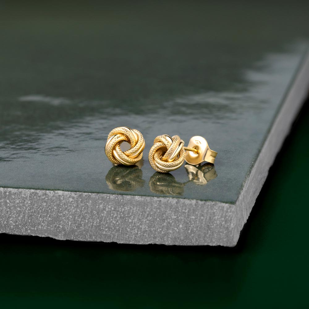 Textured gold knot studs placed ona shiny green tile showcasing its bail