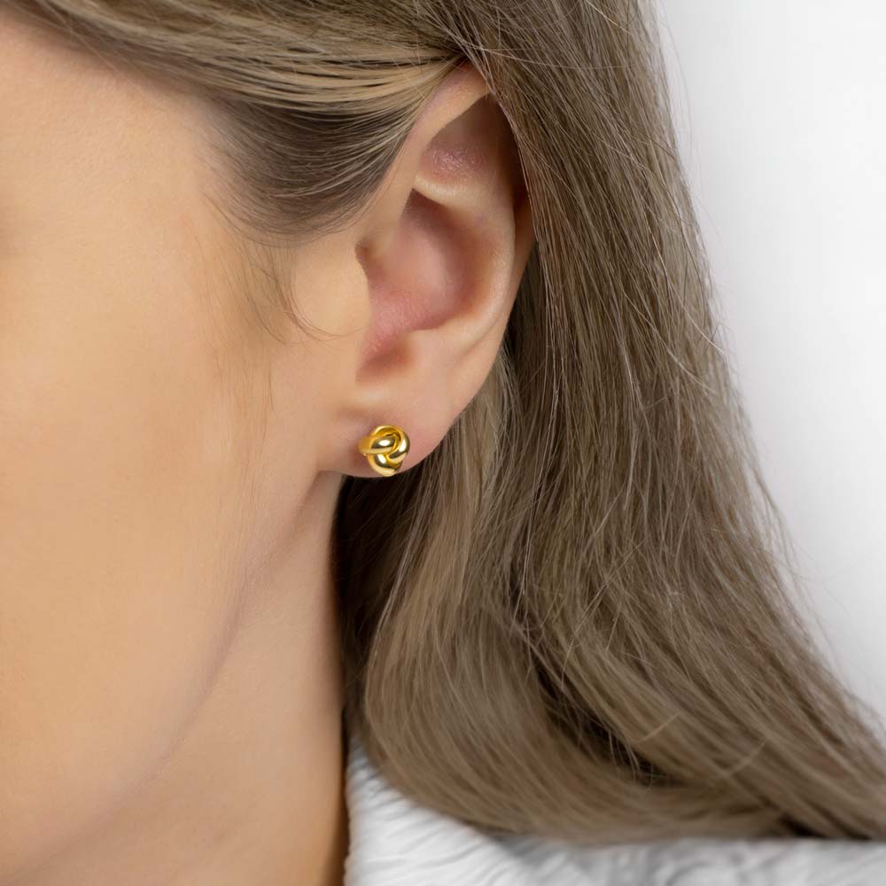 A picture of a woman wearing gold minimal knot studs earring
