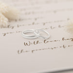 Two silver wedding rings placed on a delicate handwritten note symbolizing eternal love